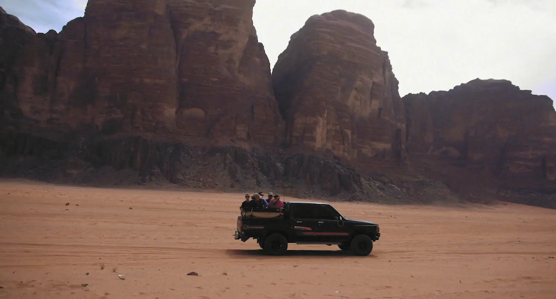 A group of people riding in the bed of a truck riding through a desert.